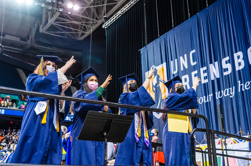 four students in graduation robes have their hands in the air